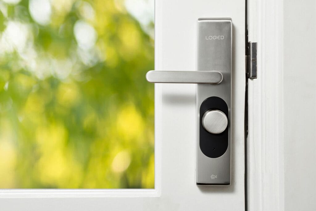 pexels-photo-6689289-6689289 Sleek smart door lock on a white door with blurred green foliage in the background.